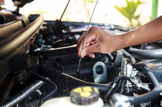 Hand pulling out oil dip stick from car hood