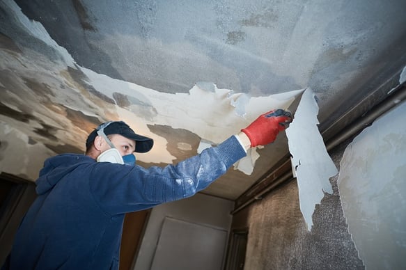 Worker removing paint from burned home ceiling