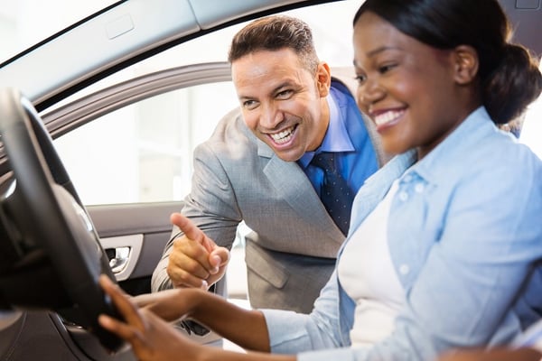 Young woman sitting in new car and talking to salesman