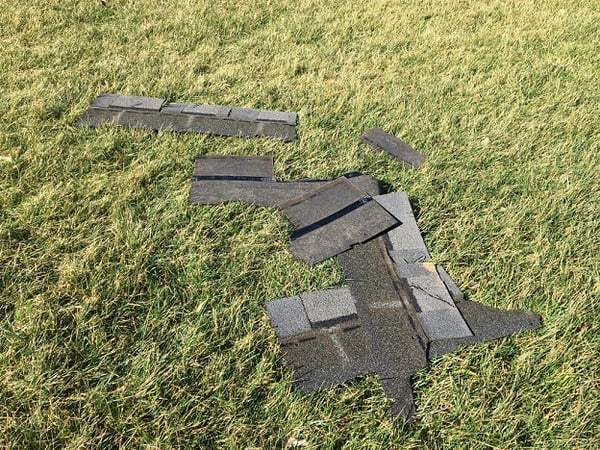 damaged roof singles on ground in front of colonial home