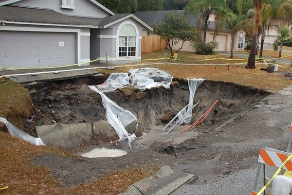 Grey and white home with large sinkhole affecting driveway and yard